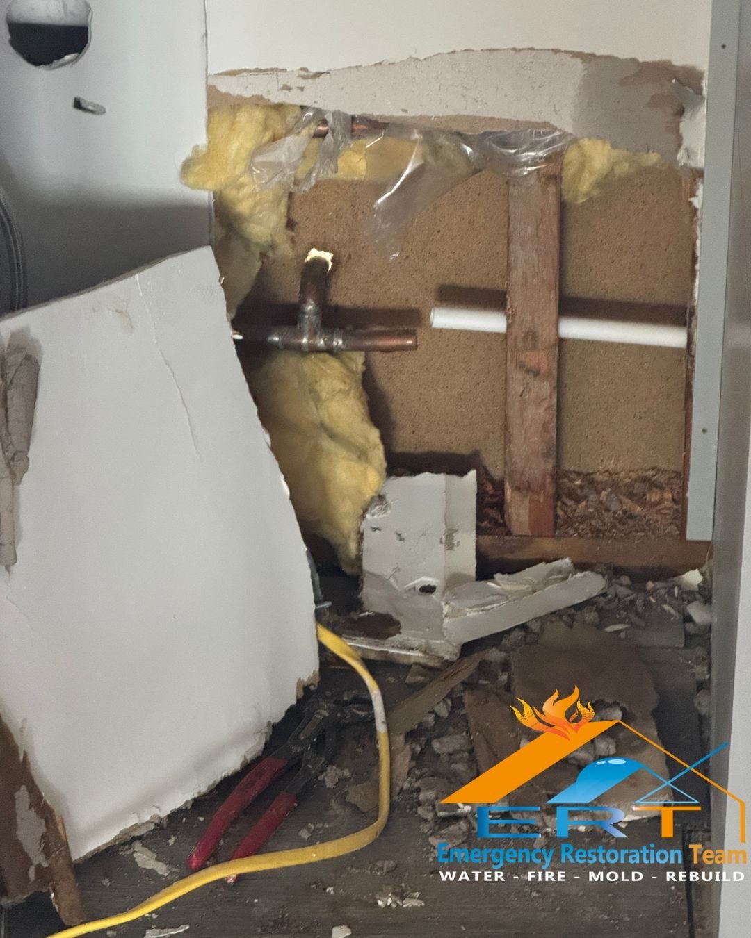 Wall cavity opened showing copper and PVC supply lines during a burst pipe repair in a Charlotte NC home